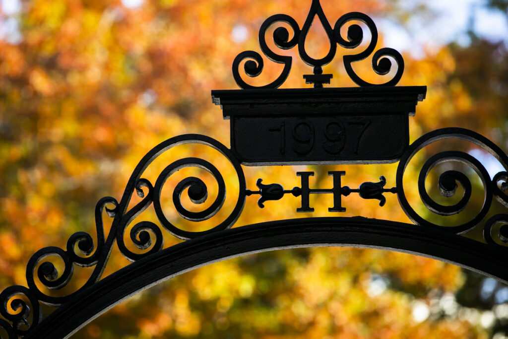 Fall leaves are on display alongside a gate decorated with an “H” at Harvard University.