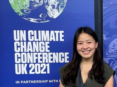 woman smiling in front of a blue banner that reads "UN CLimate Change Conference UK 2021"