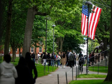 Visitors walk past the John Harvard statue and an American flag.