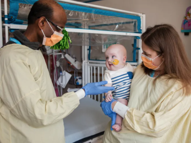 Doctors in gowns and masks stand with a baby.