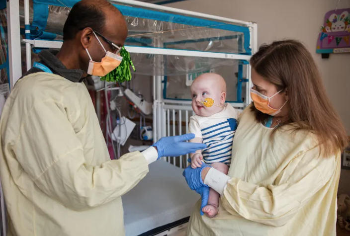Doctors in gowns and masks stand with a baby.