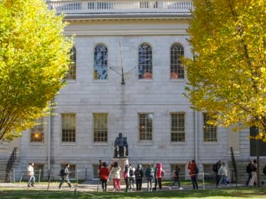 people standing in front of the John Harvard flanked by trees.