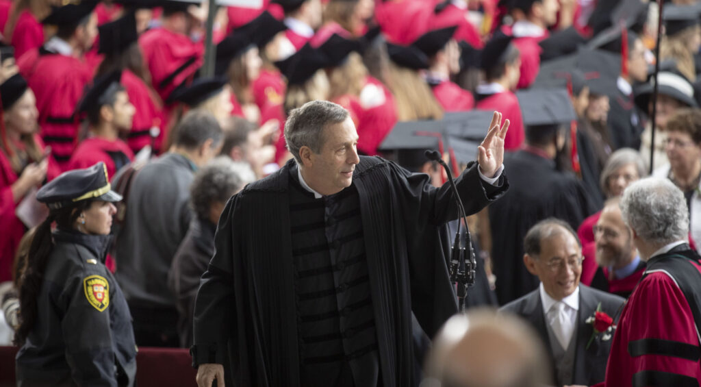 Larry Bacow waiving to a Commencement crowd