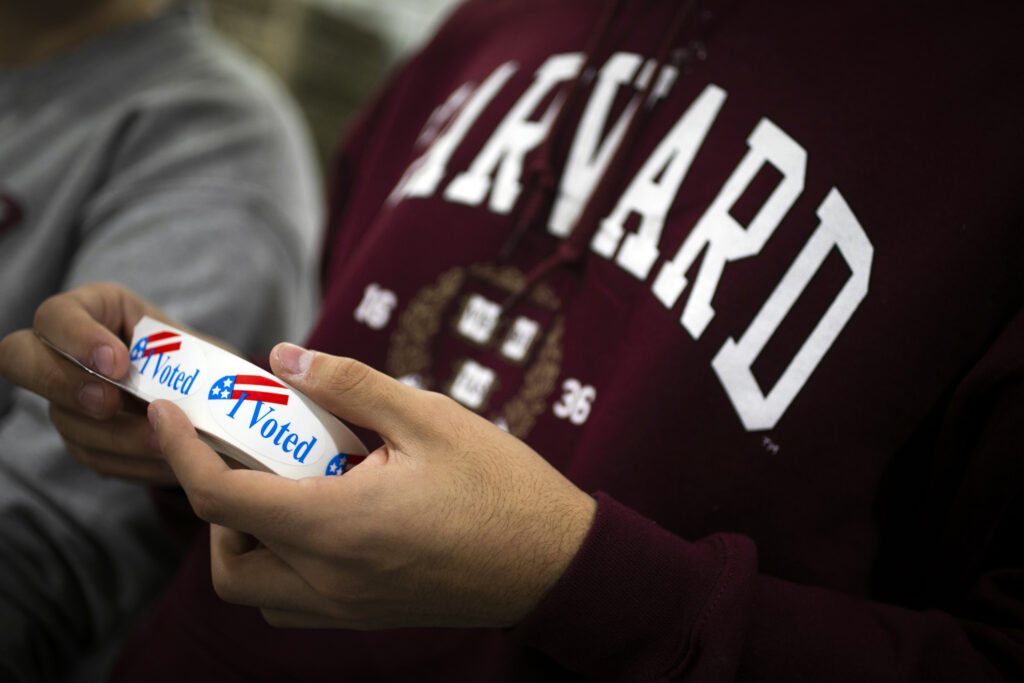 Person in a Harvard sweatshirt holds Vote stickers.