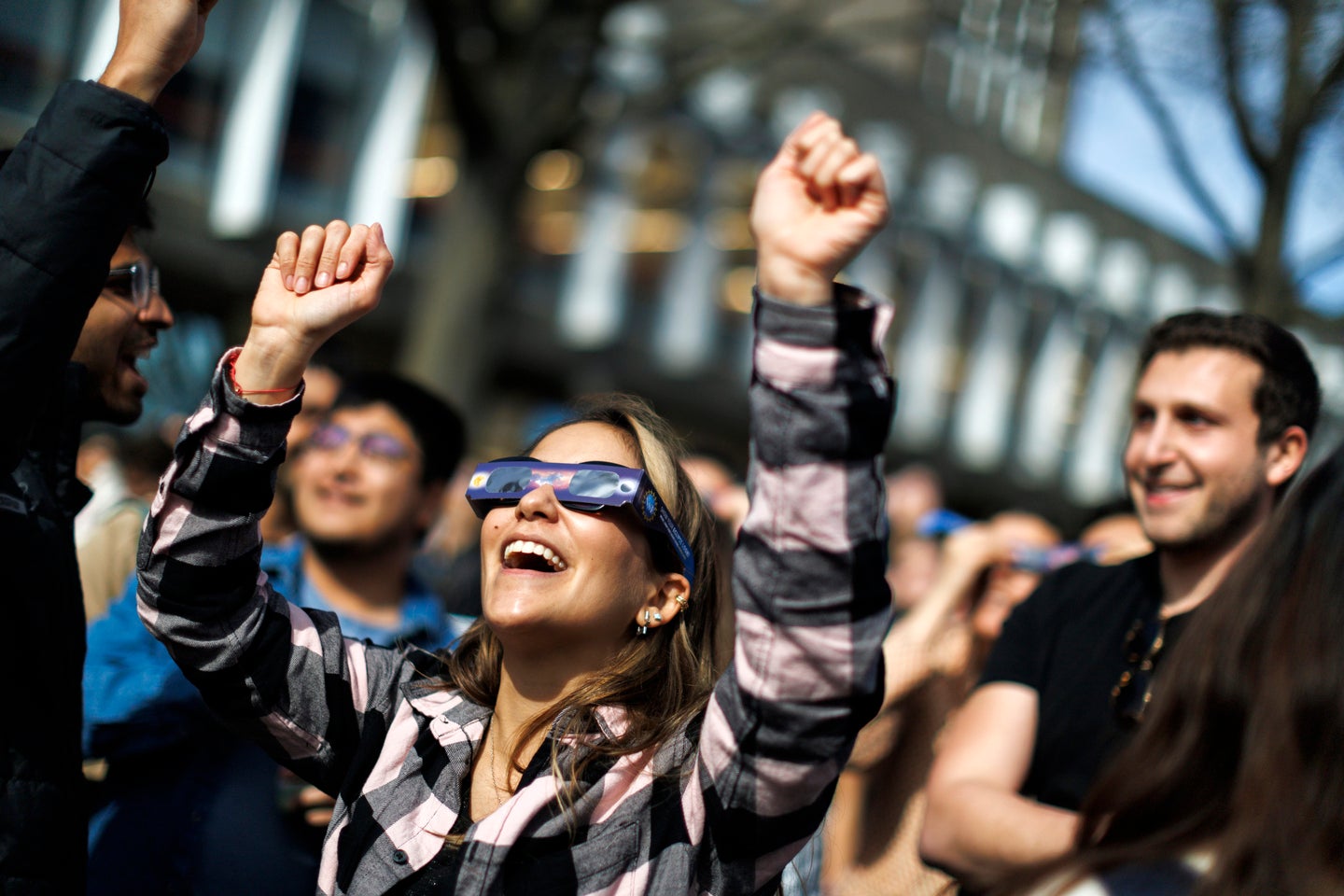 A woman wearing solar glasses raises her hands towards the sky.