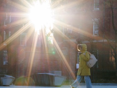 student walking across campus with a sunburst shining through two buildings.