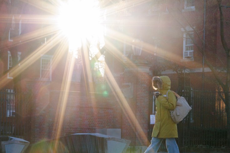 student walking across campus with a sunburst shining through two buildings.
