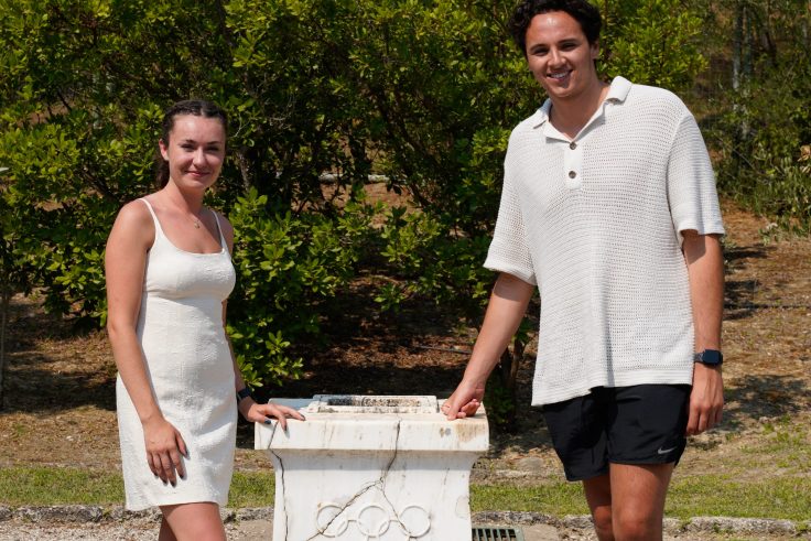 Two students standing next to a podium with Olympic rings carved into it