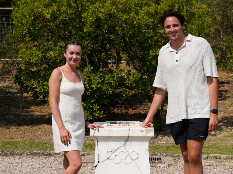 two students standing next to a podium with olympic rings carved into it