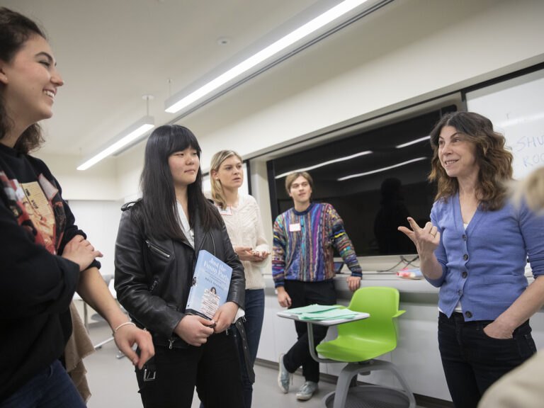 A professor standing up talking to four students.
