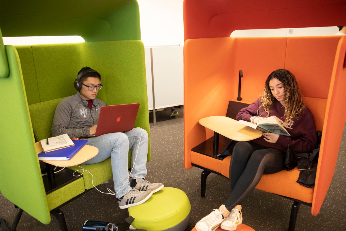 Two students study in green and orange chairs.