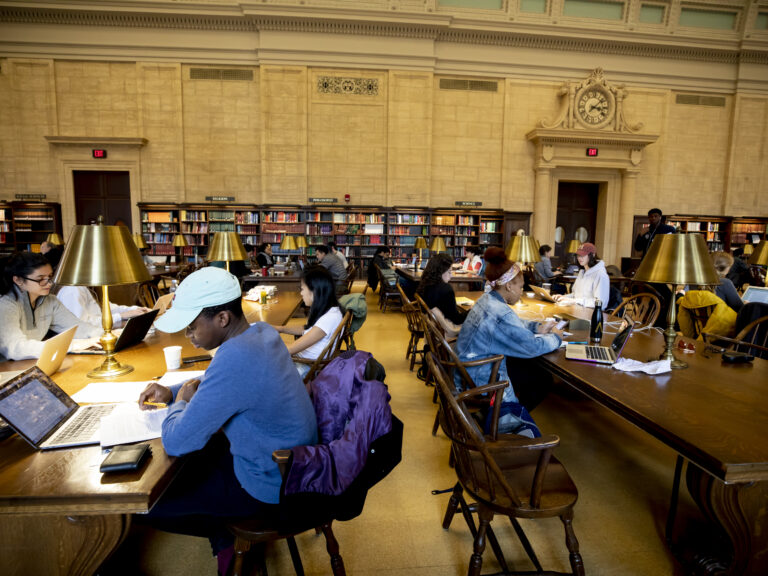 Students studying in the library at long tables.
