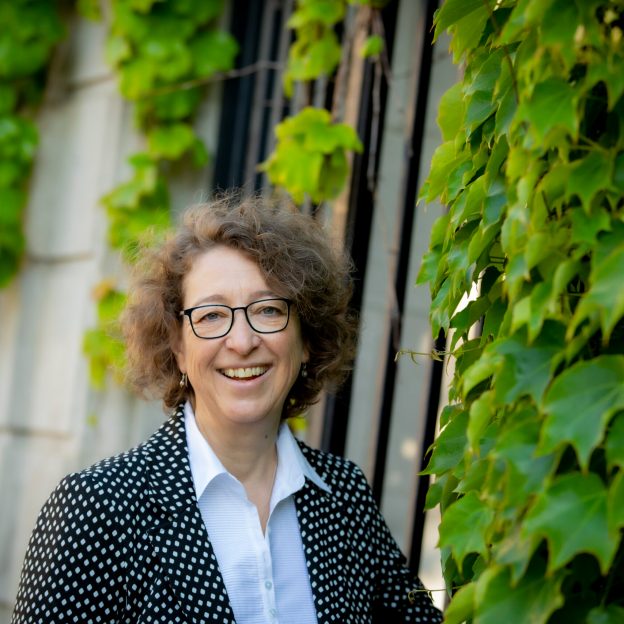 Smiling woman standing in front of ivy covered walls.