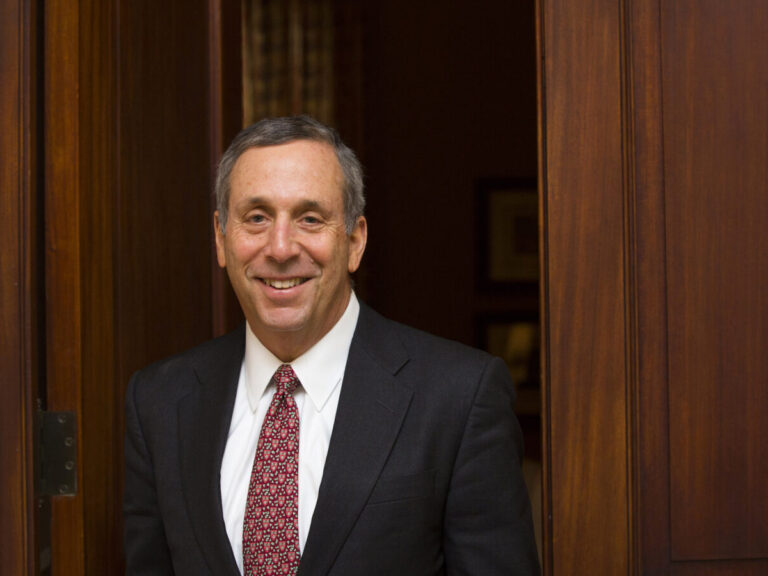A man in a suit, smiling in front of wooden doors.