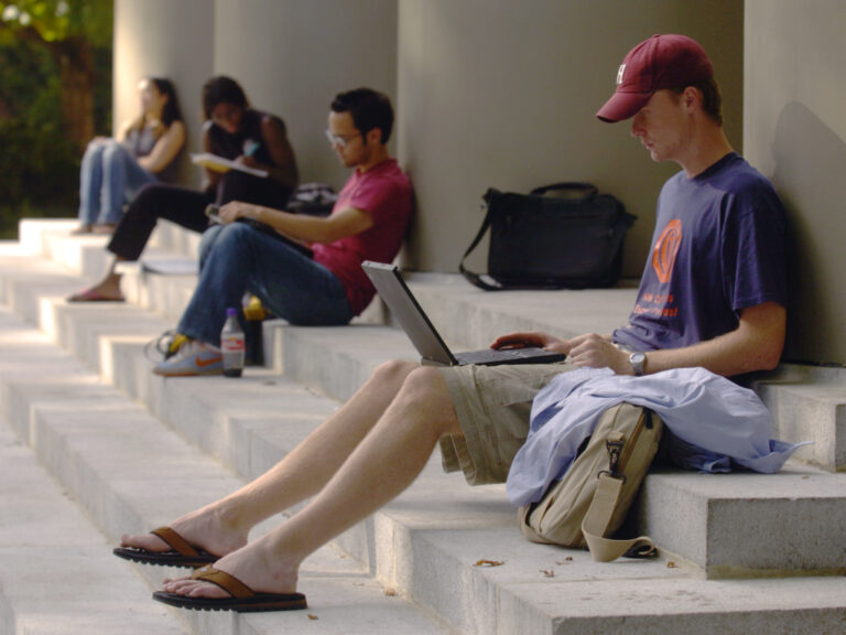 A male student sitting on steps with a laptop.