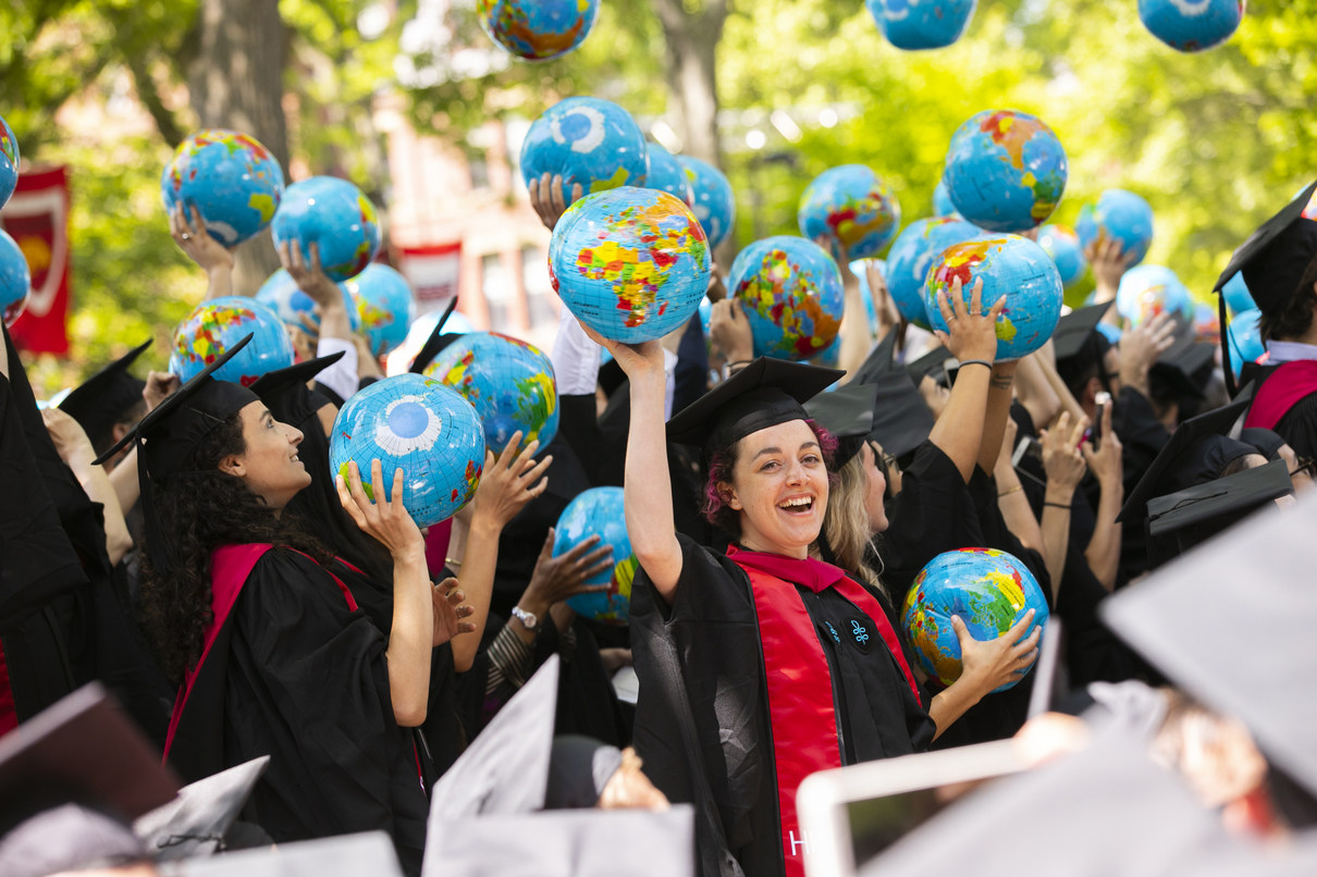 Joyous students at commencement tossing globe balls into the air.