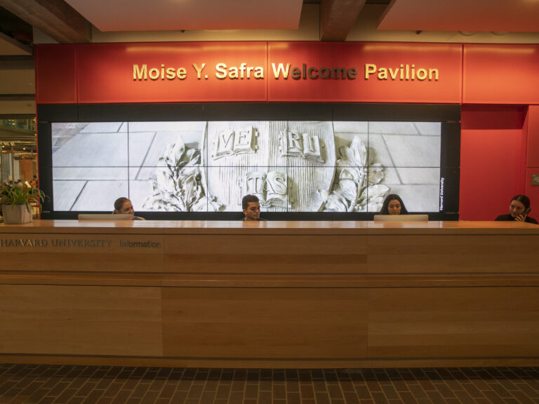 Students sitting at the information desk in front of a bright orange wall and screen.