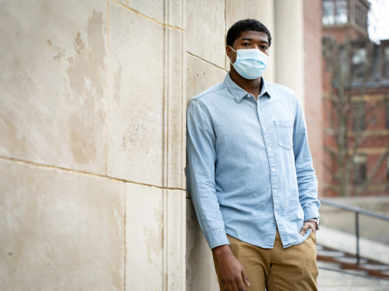A student wearing a mask stands by a white stone building