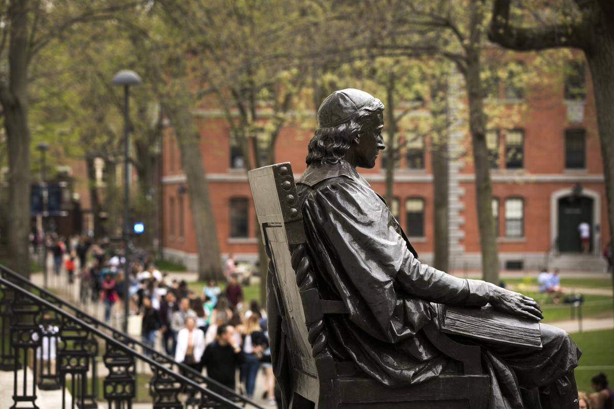People passing by John Harvard statue.