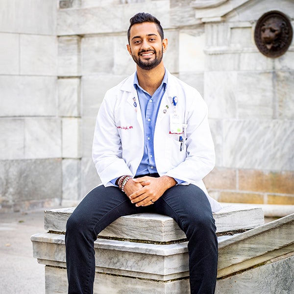 Azan Virji wears a white coat and sits outside the Medical School 
