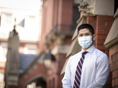A student wearing a mask stands by a brick building