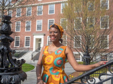 A student wearing a brightly colored dress stands on the Harvard campus