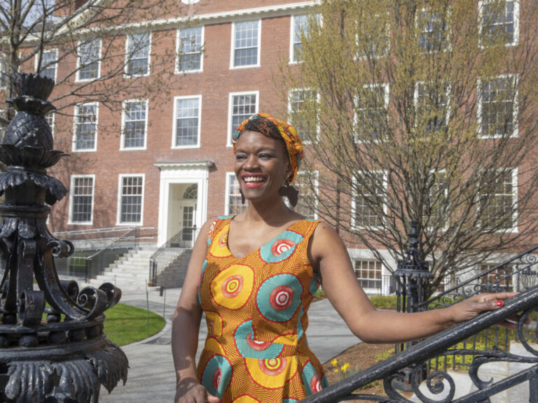 A student wearing a brightly colored dress stands on the Harvard campus