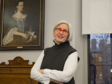 A woman stands with her arms crossed by a historic portrait