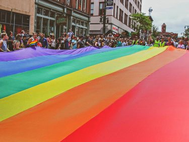 A crowd holds a huge rainbow flag