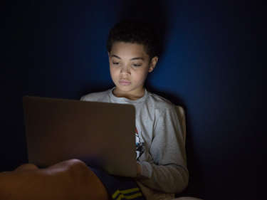 A young student looking at a laptop in the dark