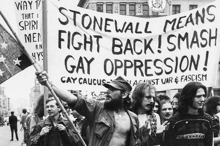 A black and white photo of protesters with a sign that reads, "Stonewall means fight back! Smash gay oppression!"