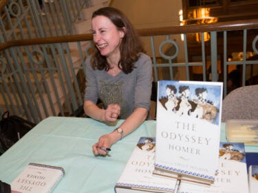 A woman sits at a table with copies of a book entitled "The Odyssey" next to her