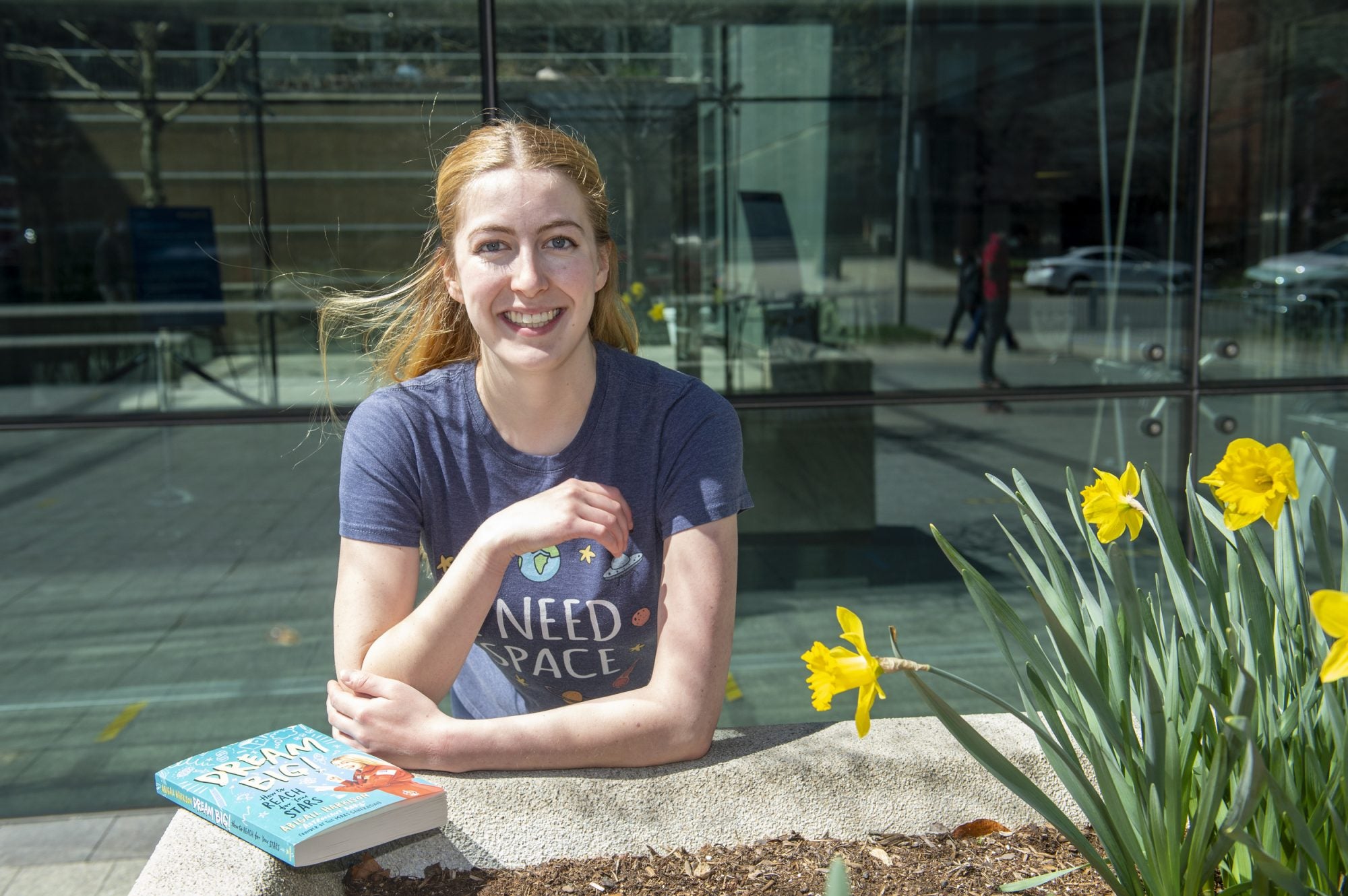 A woman sits outside beside flowers with a book "Dream Big" in front of her