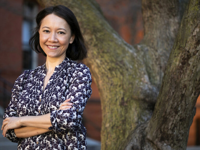 A woman stands with her arms crossed in front of a tree