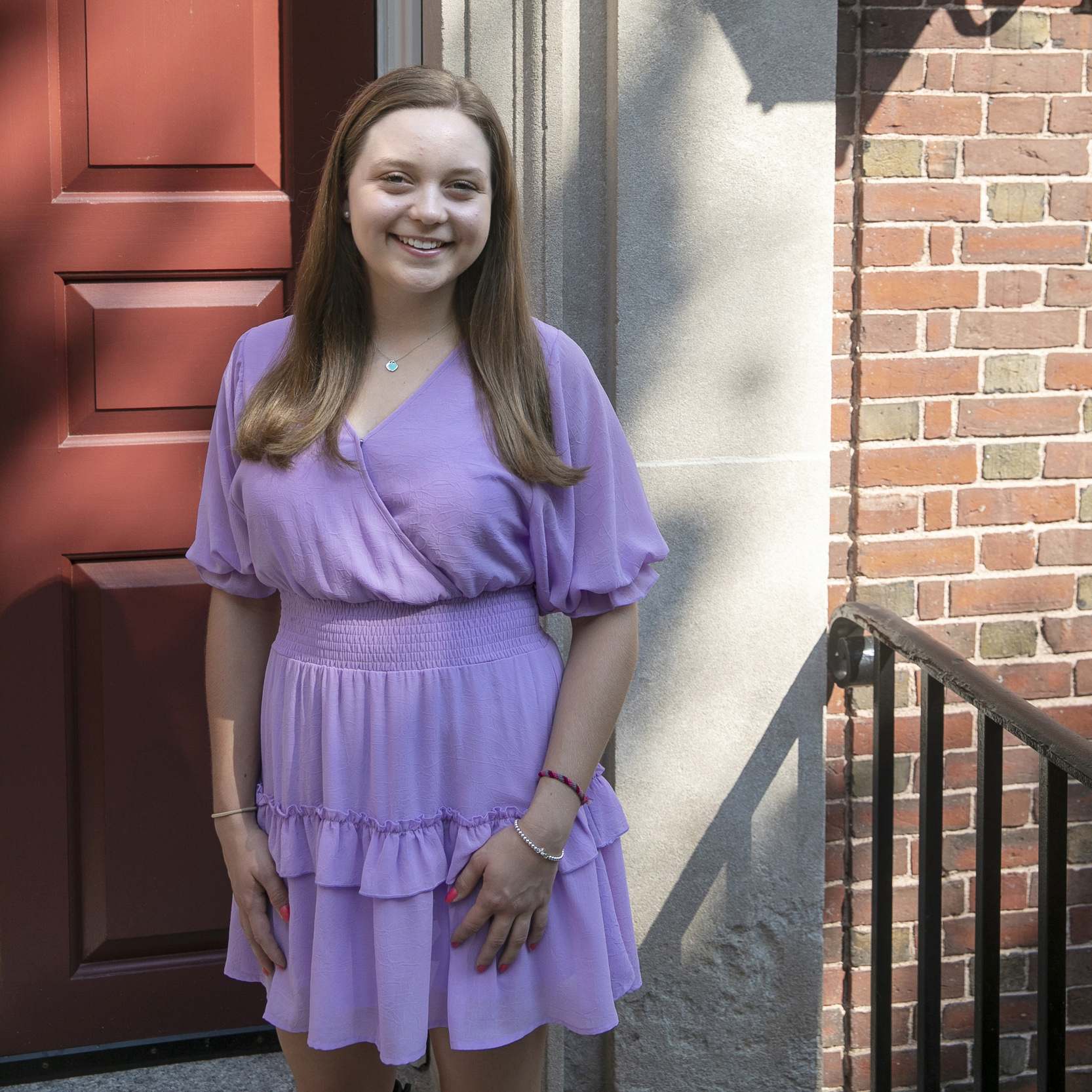 A student stands in front of a red door of a brick building