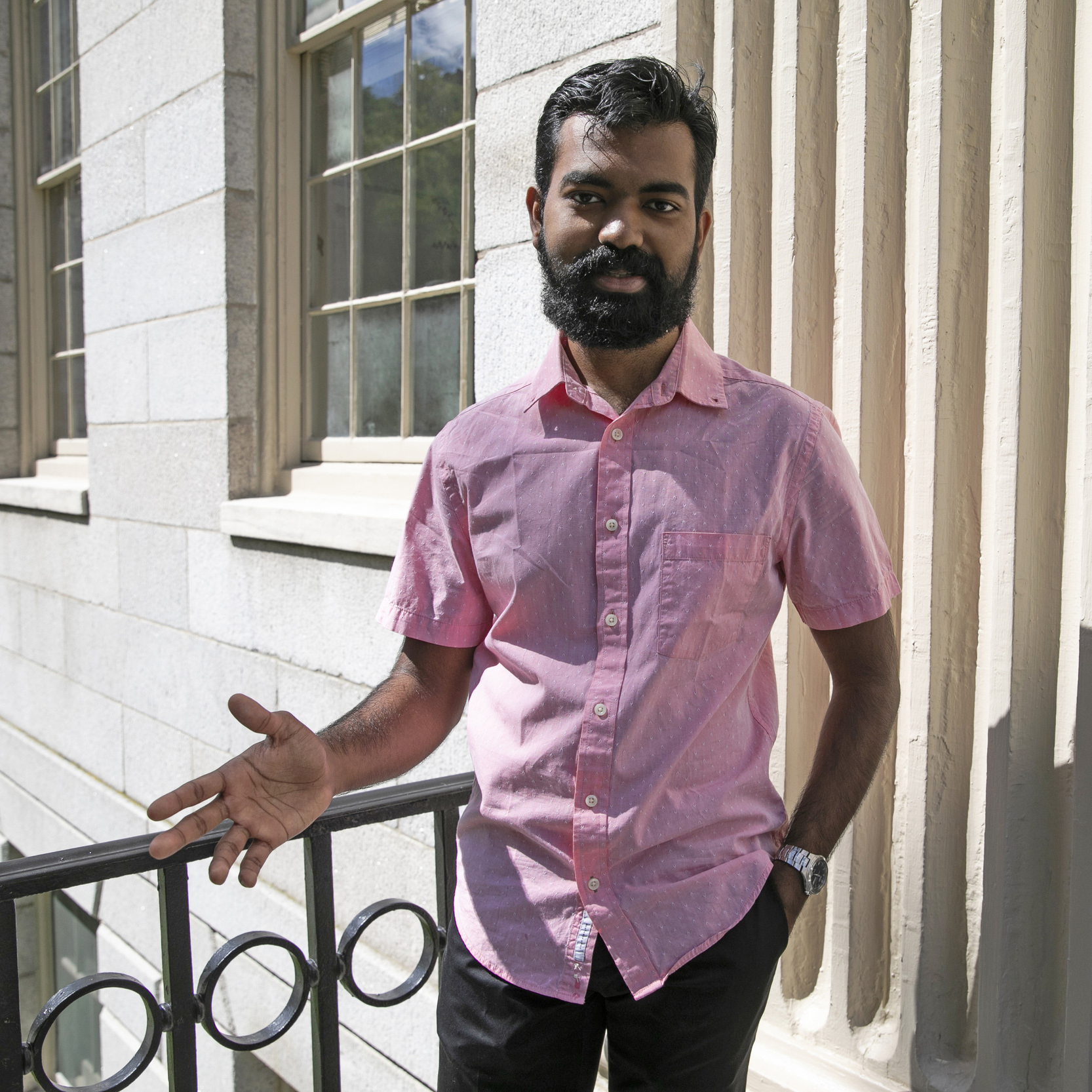 A student stands in front of a stone building with a black iron railing