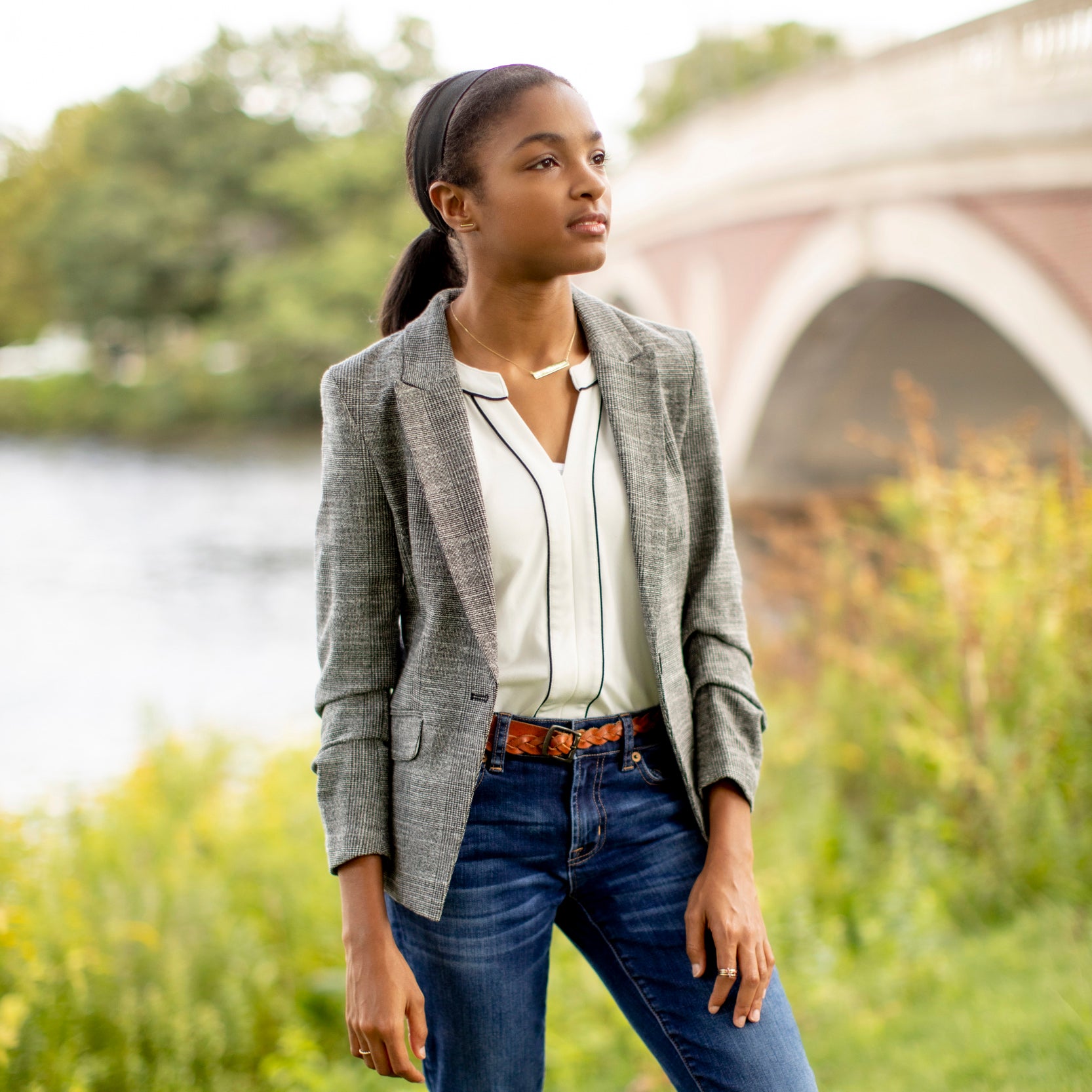 A student stands outside near a river and bridge
