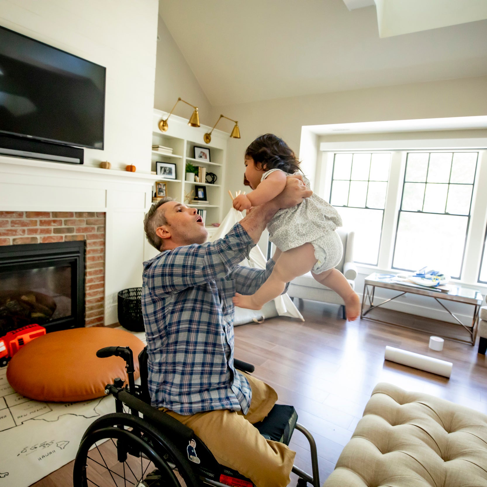 A man using a wheelchair raises his infant daughter in the air