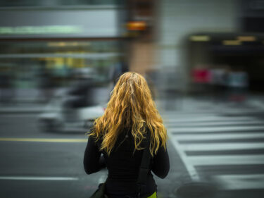 A woman stands with her back to the camera, facing a busy street