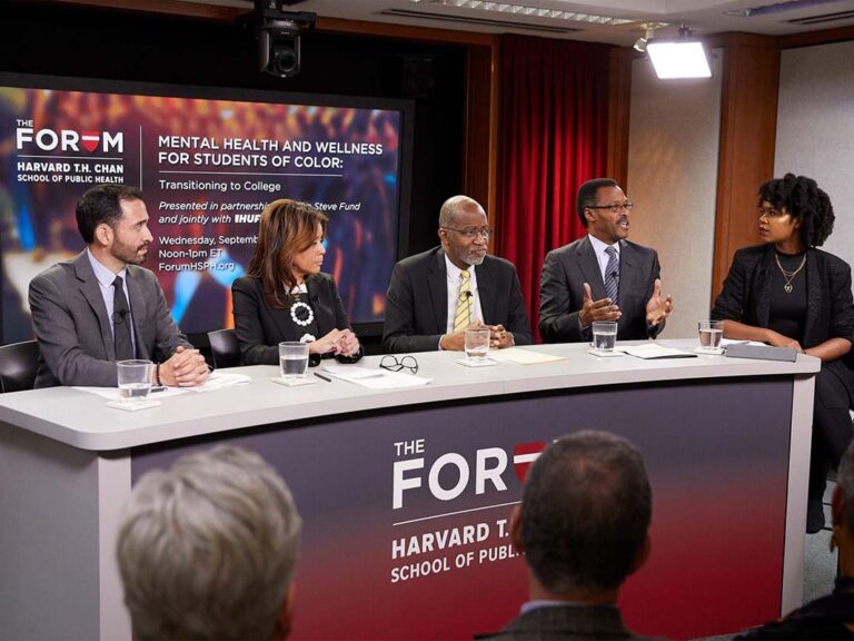 Four panelists sit at a newsroom type of desk at the Harvard Chan School