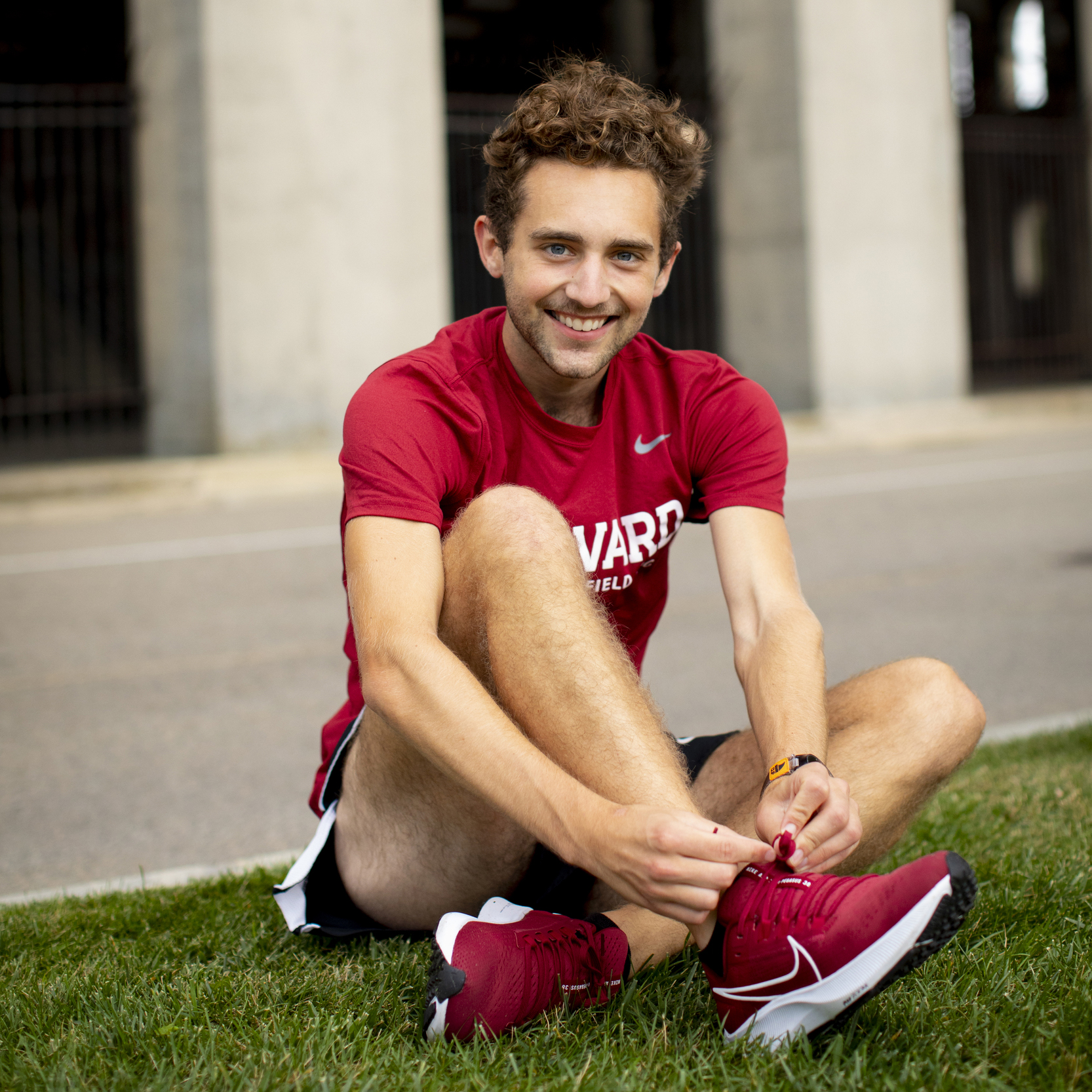 A student athlete ties his shoe while sitting on the grass