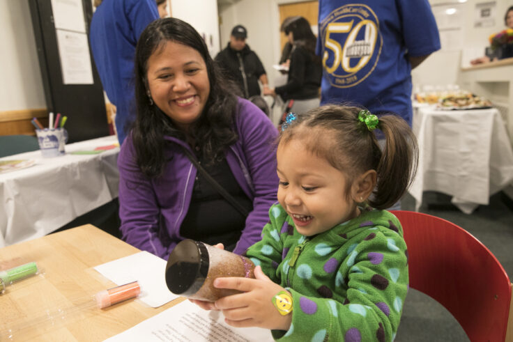 A mom looks on as her daughter holds a toy