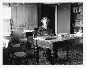 older photograph of a woman sitting at a desk.