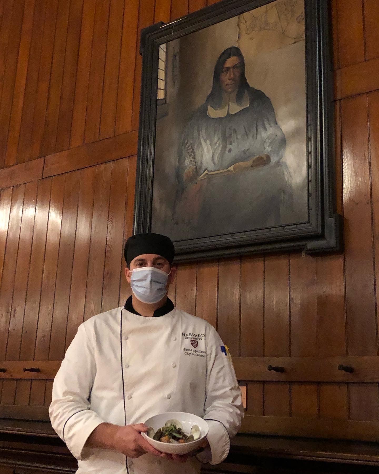A chef standing in front of a portrait of a Native American