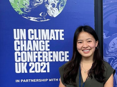 A student stands in front of a sign that reads "UN Climate Change Conference UK 2021"