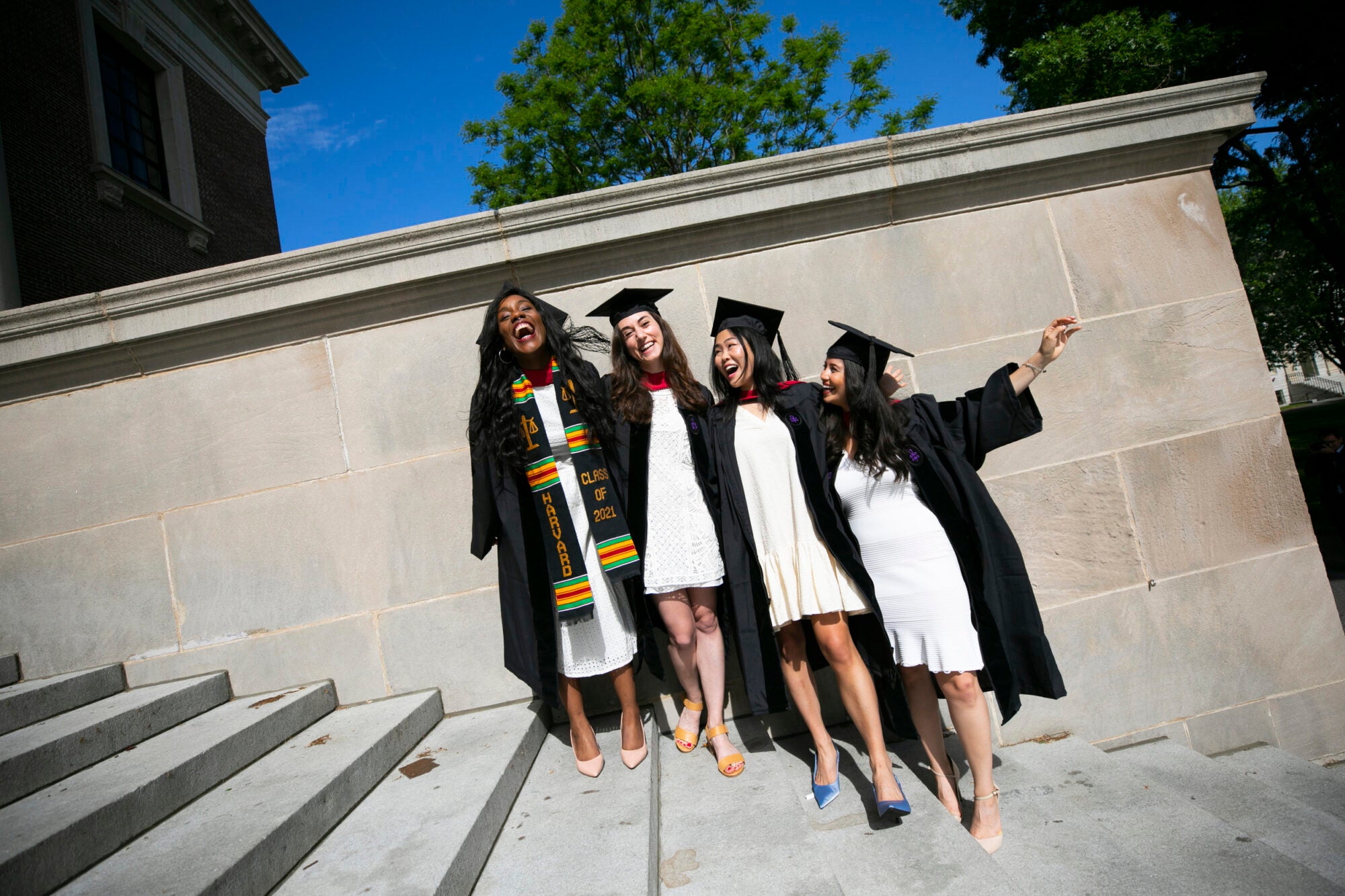 Four students in caps and gowns stand together for a photo on stone steps