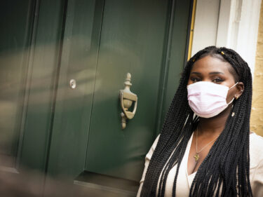 A student wearing a mask stands in front of a green door