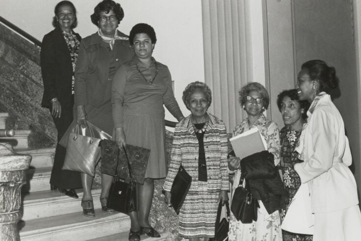 A black and white photo of 7 Black women standing by stairs