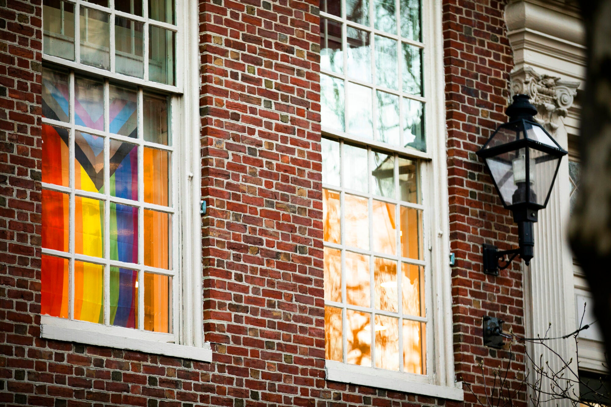 A pride flag hangs in the window of a brick building
