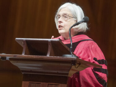 A woman wearing a red commencement robe speaks at a podium